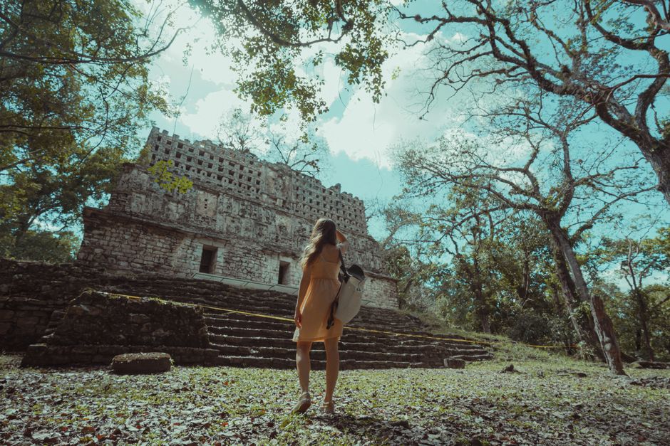 A woman stands before ancient Mayan ruins in a tranquil forest setting in Mexico.