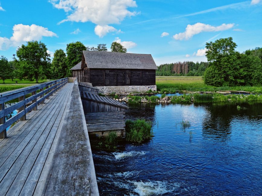 Scenic landscape featuring a historic wooden watermill and footbridge in Estonia's countryside.