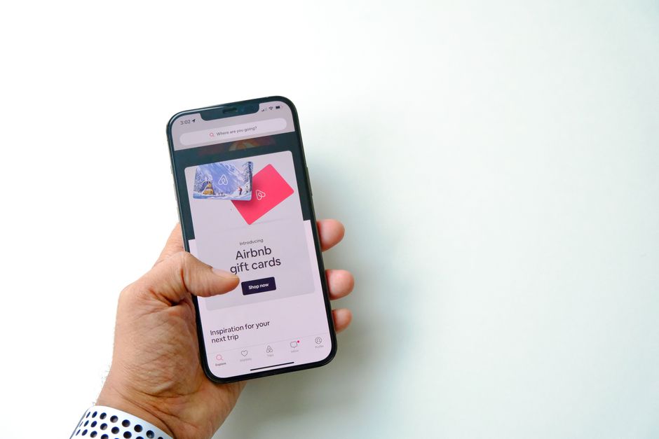 Close-up of a hand holding a smartphone displaying Airbnb gift cards on a white background.