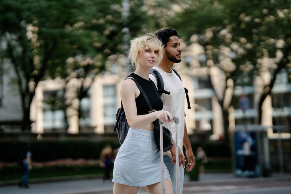 A young couple enjoys a sunny day walking in an urban park with lush green trees.