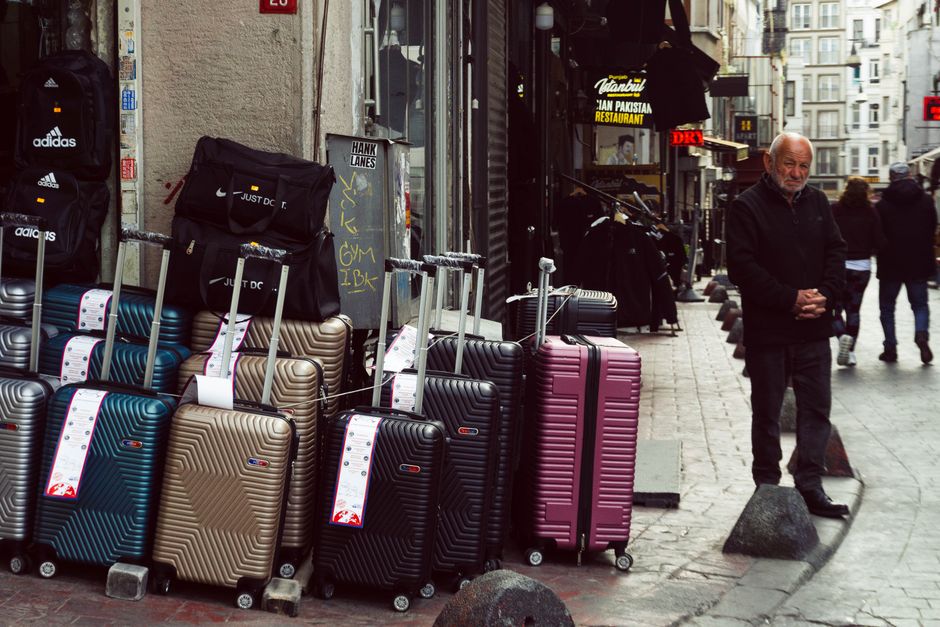 A man stands beside a colorful display of luggage on a bustling street in Istanbul, Turkey.