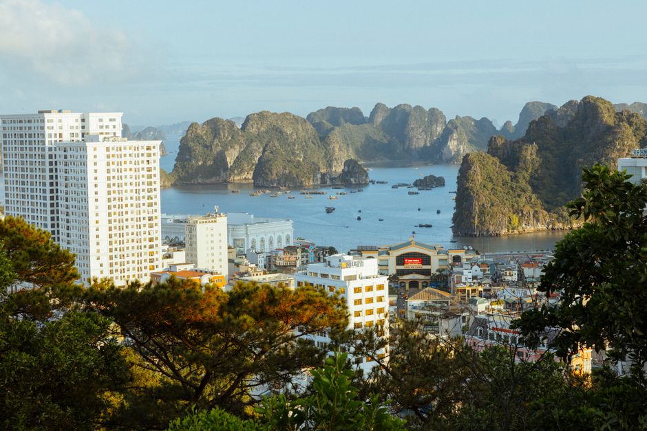 View of Ha Long Bay with tall buildings and iconic limestone karsts at sunrise.