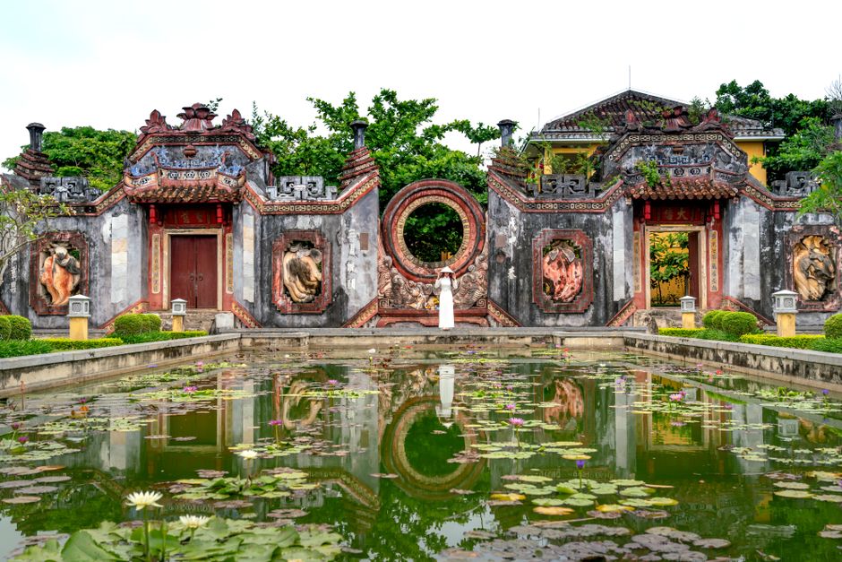Scenic view of a historic temple facade with a tranquil pond and lotus flowers.
