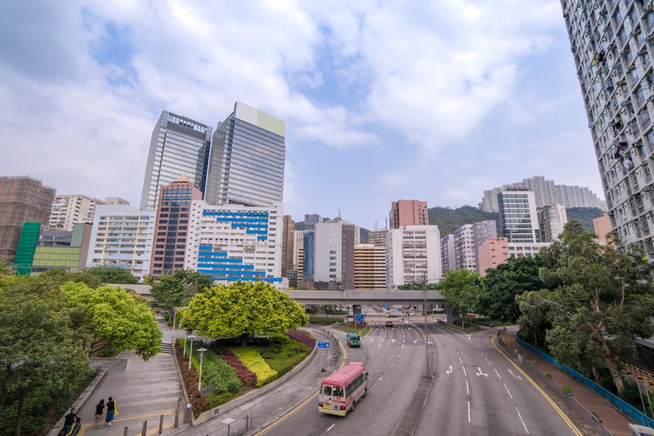 Wide-angle view of a Hong Kong cityscape featuring skyscrapers, greenery, and a vibrant road.