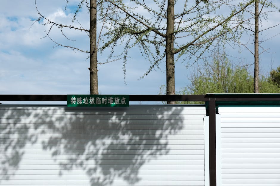 A metal fence casting shadows with trees in the background under a clear sky.