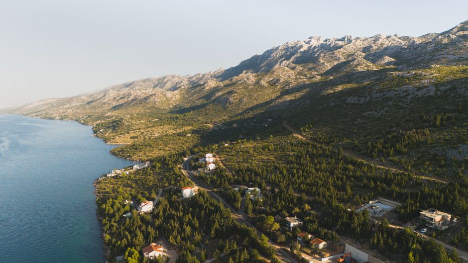 Aerial view of a mountainous coastal landscape with lush greenery and scattered houses.