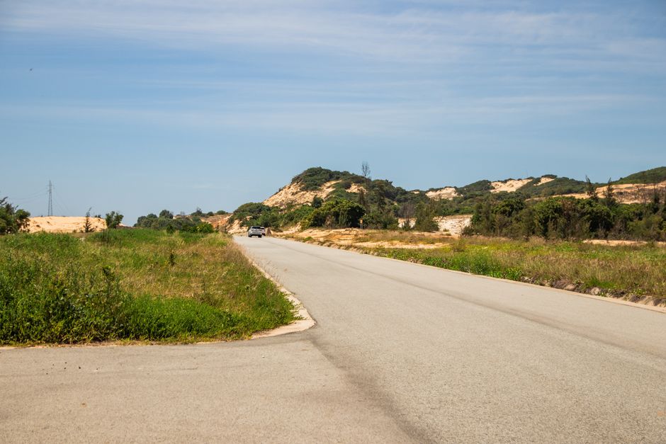 A scenic view of a rural road surrounded by lush greenery and hills in Phan Thiết, Vietnam.
