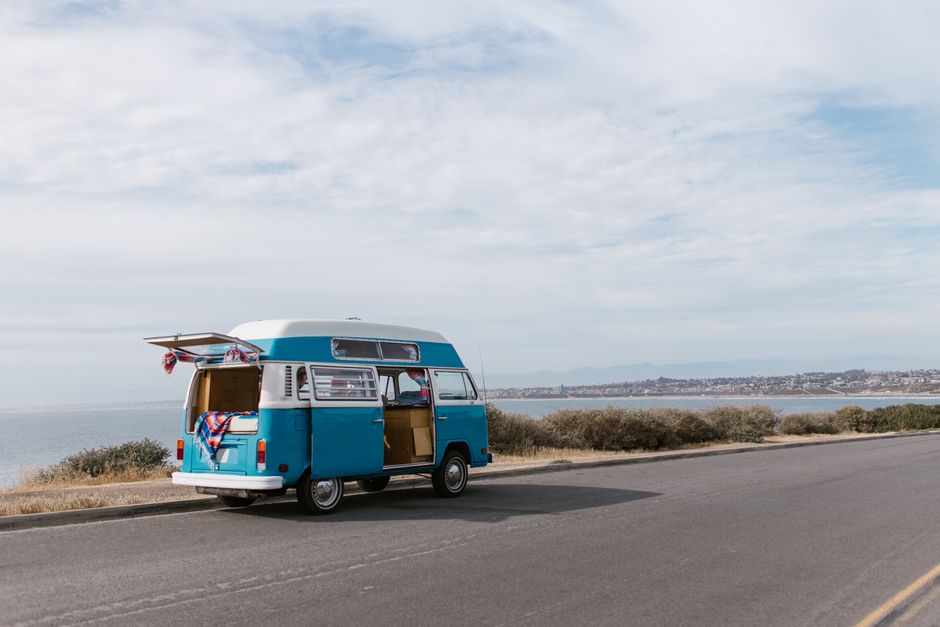 A classic blue van parked along a scenic coastal road under a cloudy sky.