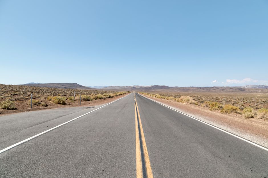 A straight empty road through a vast desert landscape under a clear blue sky.