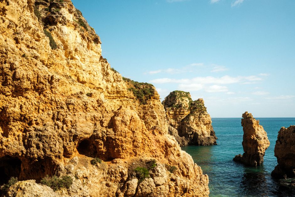 Dramatic rock formations and clear waters at Algarve coastline on a sunny day.