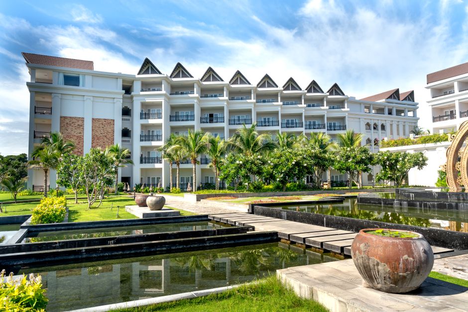 A luxurious resort featuring modern architecture surrounded by lush palm trees and tranquil pond.