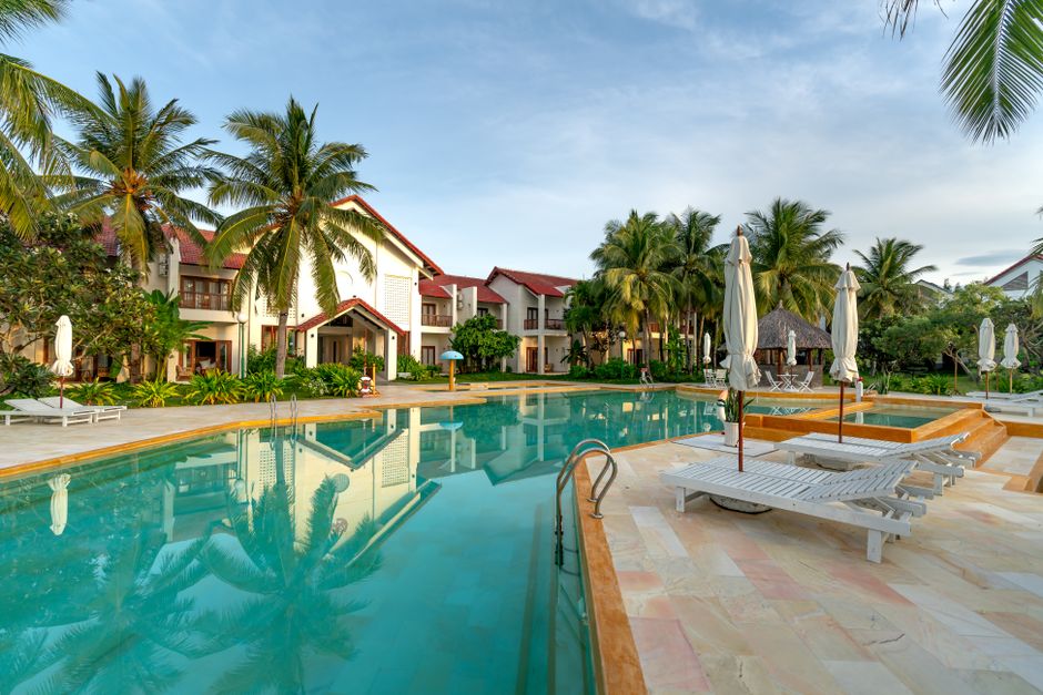A tranquil resort poolside scene with palm trees and white beach chairs for relaxation.