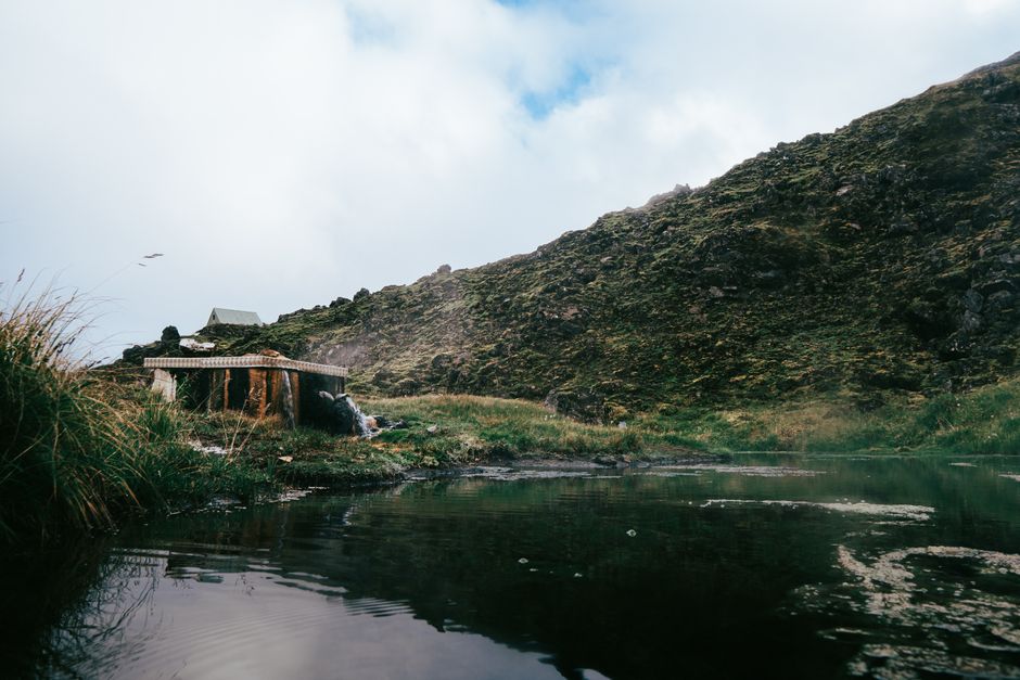 Tranquil mountainous scene in Iceland with a reflective pond and lush greenery.