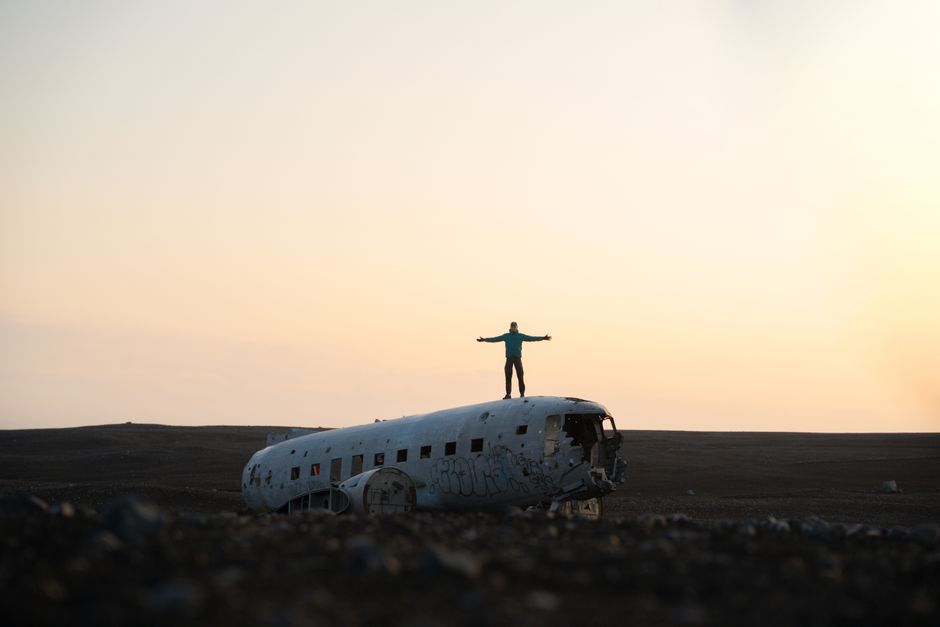 A person stands atop the famous Solheimasandur plane wreck in Iceland at sunset.
