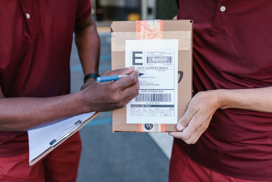 Courier signing package delivery receipt on a clipboard outdoors.