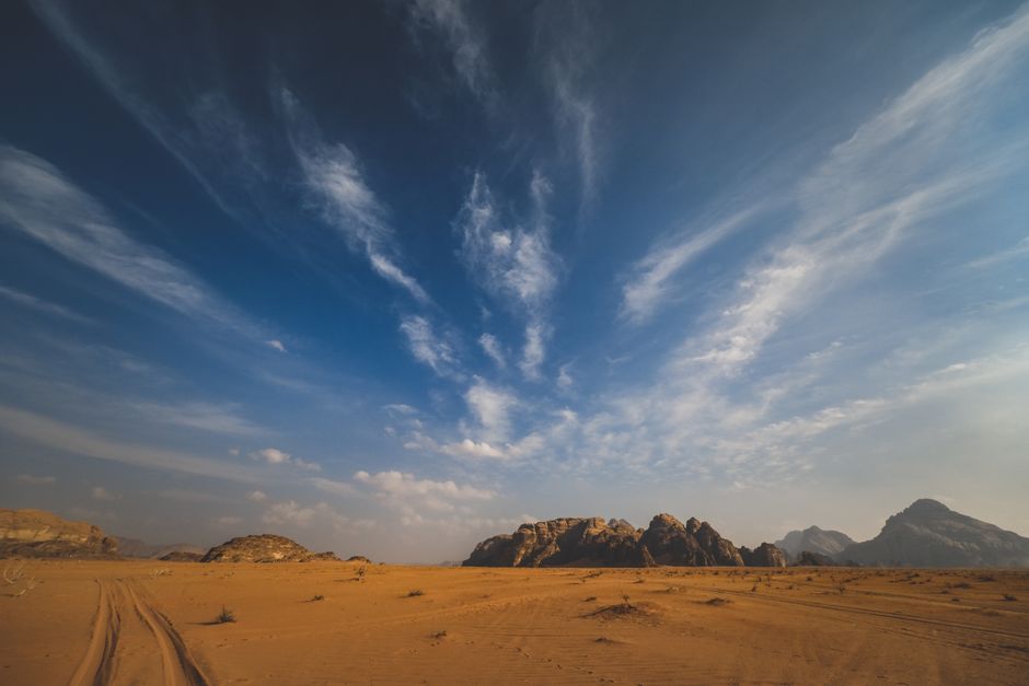 Expansive desert scene with rugged rocks and wispy cirrus clouds under a vibrant blue sky.
