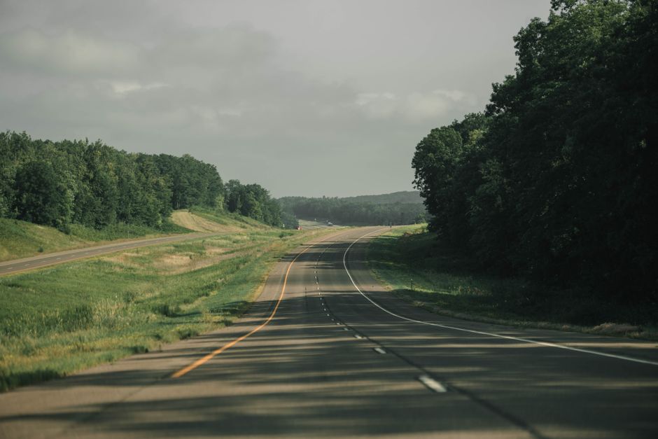 A peaceful highway running through lush greenery in Minnesota under a cloudy sky.