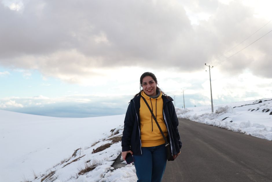 A cheerful young woman enjoying a winter day on a snow-covered road under a dramatic cloudy sky.