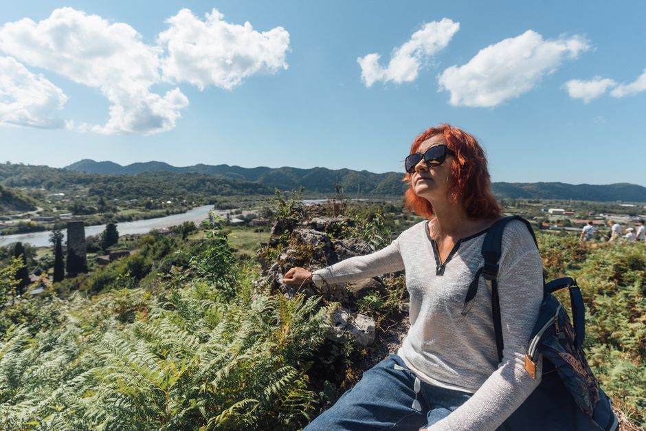 A woman enjoys a sunny mountain view in Гагра, capturing the essence of adventure and travel.