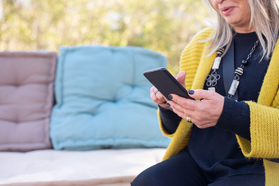 Middle-aged woman using a smartphone outdoors with colorful cushions.