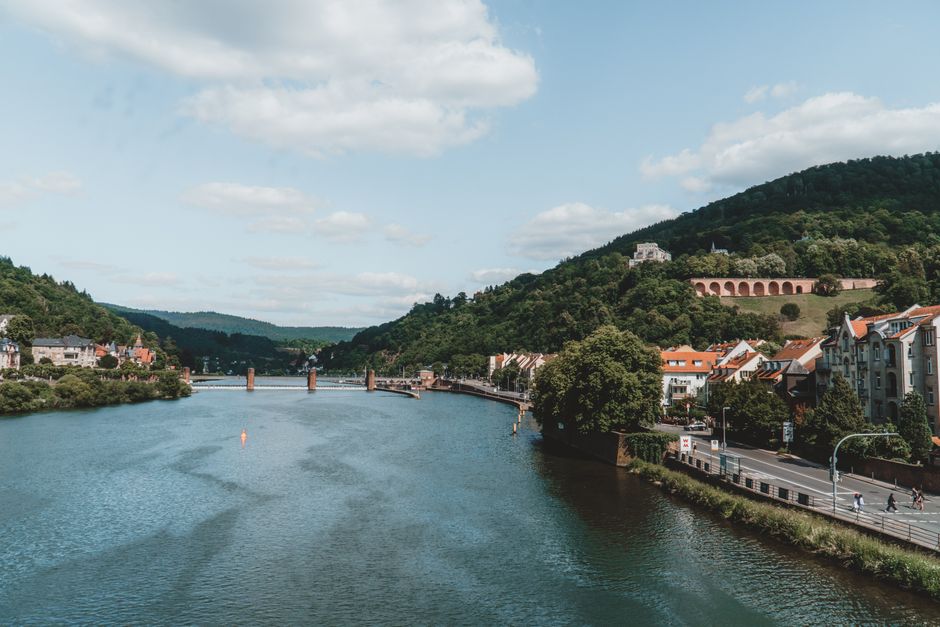 Picturesque scene of Heidelberg's Neckar River and historic bridge, surrounded by lush hills.