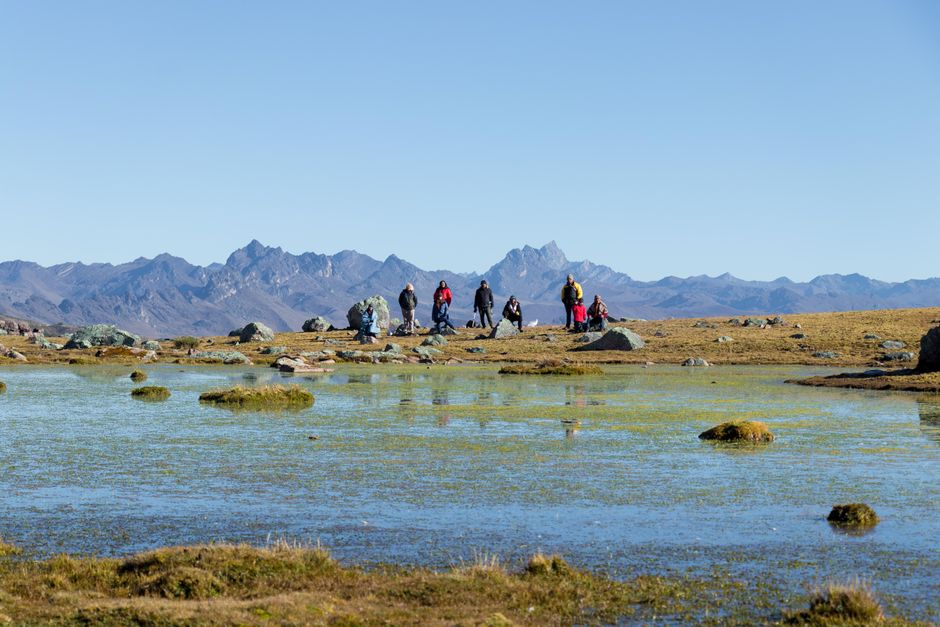 Group of hikers exploring a serene mountain landscape with a clear sky reflecting on a lake.