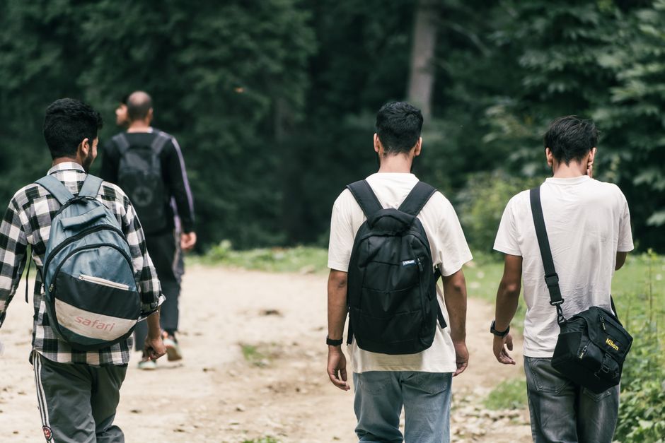 Group of young men hiking with backpacks through a lush forest trail.