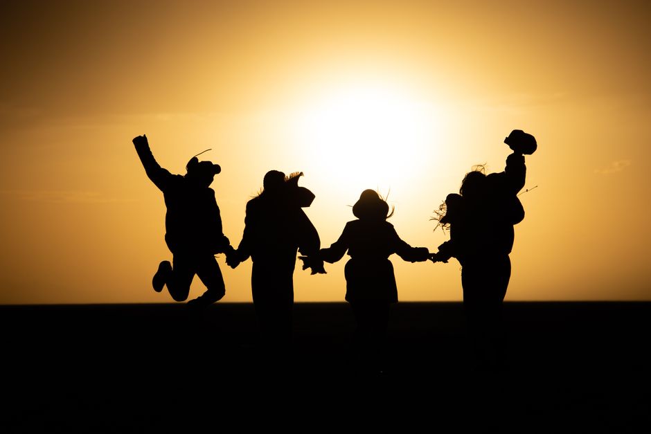 Silhouette of friends jumping and holding hands against a stunning sunset in Shahrud, Iran.