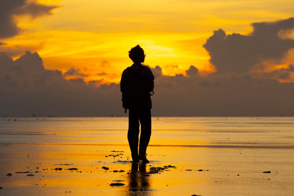 A lone traveler silhouetted against a vibrant sunset on a serene beach.