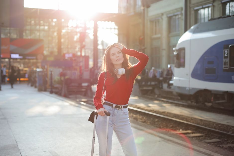Sensual female with suitcase standing on railway platform and looking at camera while waiting for train