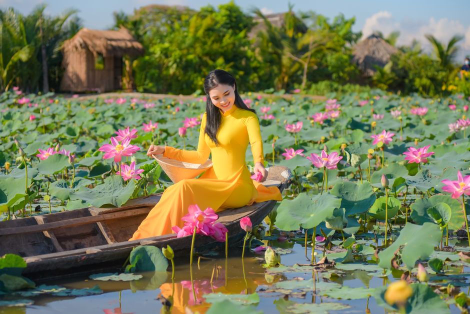 Beautiful woman in a vibrant yellow dress sitting on a boat surrounded by blooming lotus flowers.