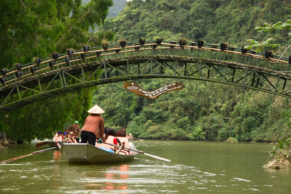 A peaceful boat ride under a scenic bridge in a lush, green Asian landscape. Captures tranquility.