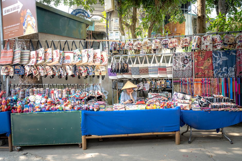 Colorful market stall in Vietnam featuring bags and textiles under trees.