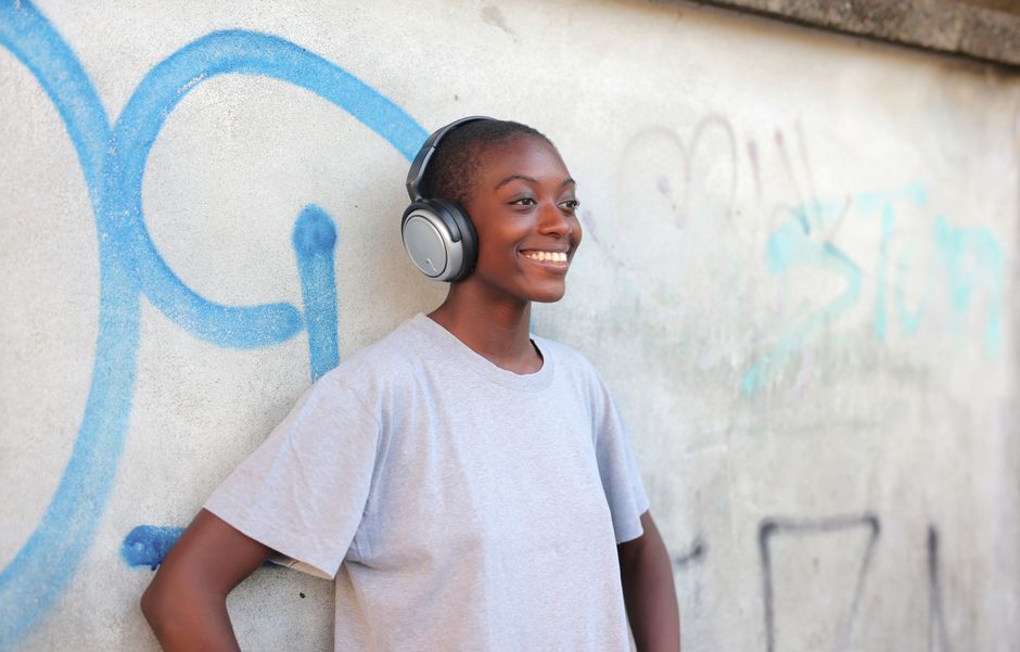 A cheerful woman in headphones leans against a graffiti-covered wall, enjoying music.