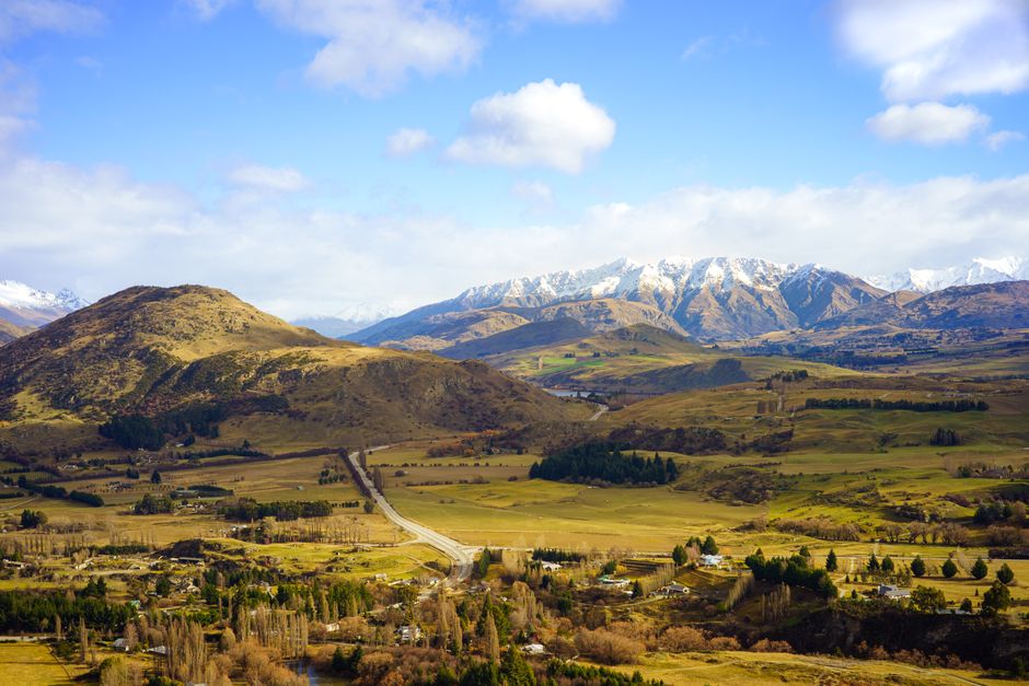 Breathtaking aerial view of Queenstown's rural landscape with hills and snow-capped mountains.