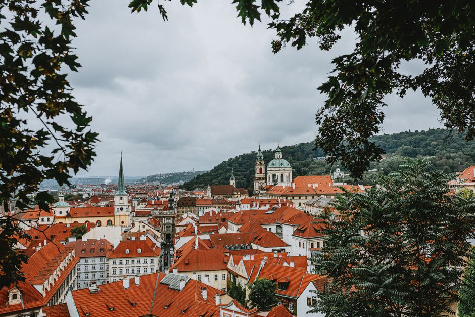 Beautiful view of Prague's historic red rooftops framed by lush greenery under a cloudy sky.