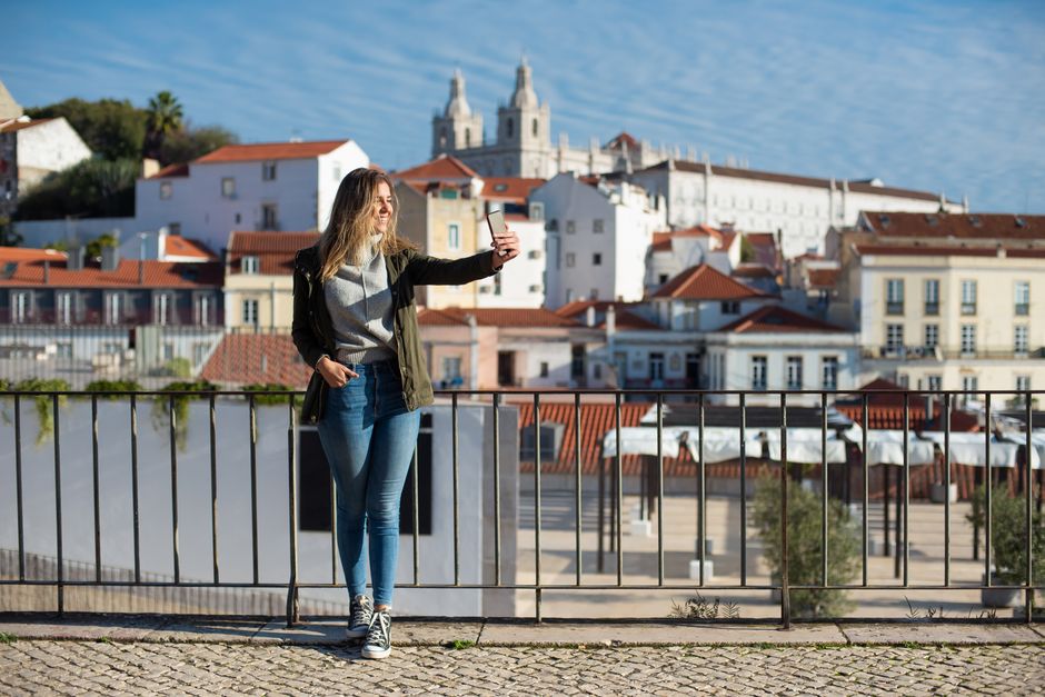A woman takes a selfie with the scenic backdrop of Lisbon architecture.