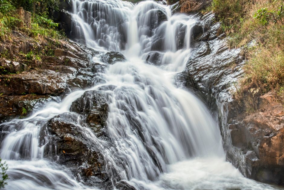 Dramatic waterfall cascading over rocks in a green forest, showcasing natural beauty.