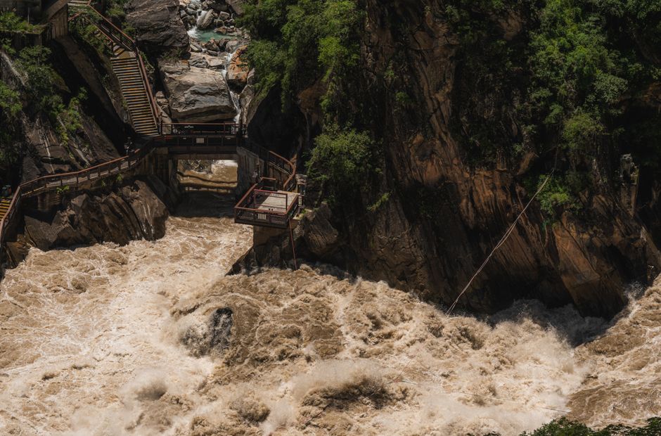 Dynamic photo of turbulent river rapids crashing through a gorge, flanked by wooden pathways and lush greenery.